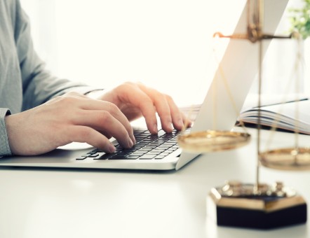 Person tippt auf Laptop, im Vordergrund eine goldene Justitia-Waage – Symbolbild für eine Rechtsschutzversicherung